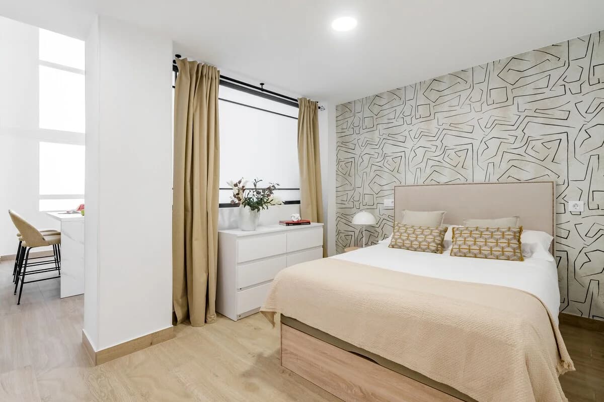 Main bedroom with graphic wallpaper feature wall and warm linen tones