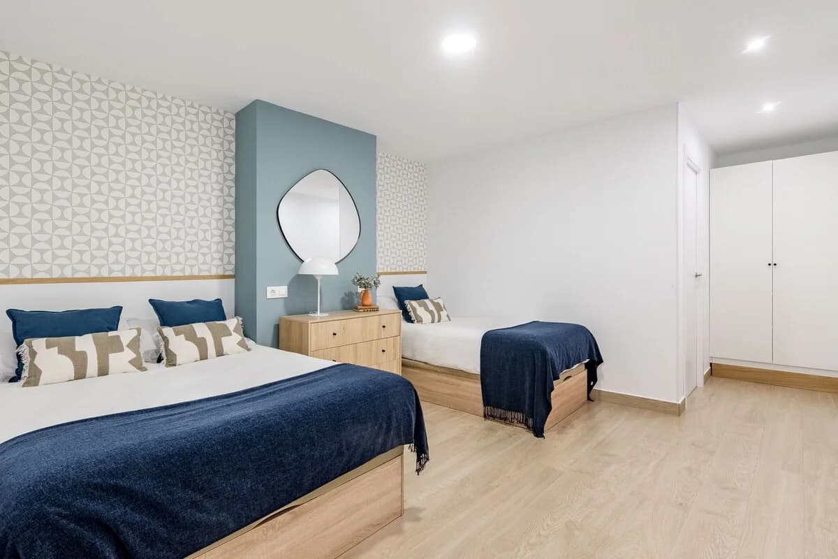 Twin bedroom with geometric wallpaper, blue accent wall and pebble mirror