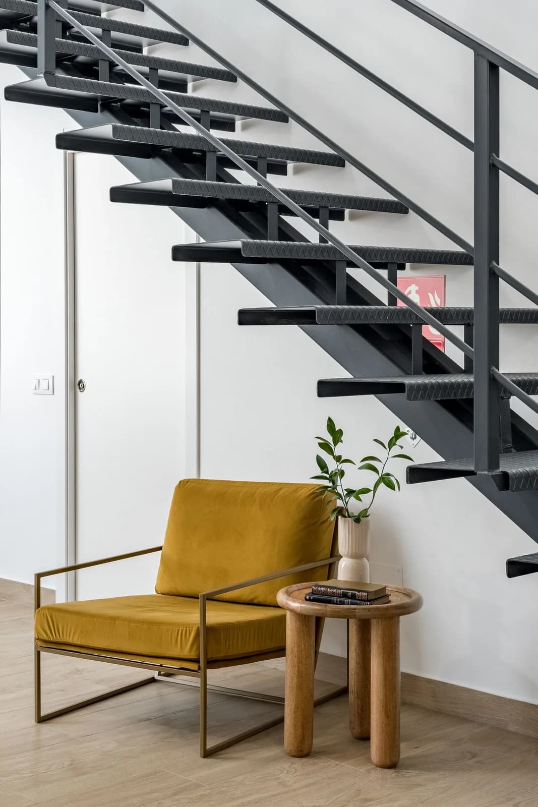 Mustard velvet chair tucked beneath a black industrial staircase
