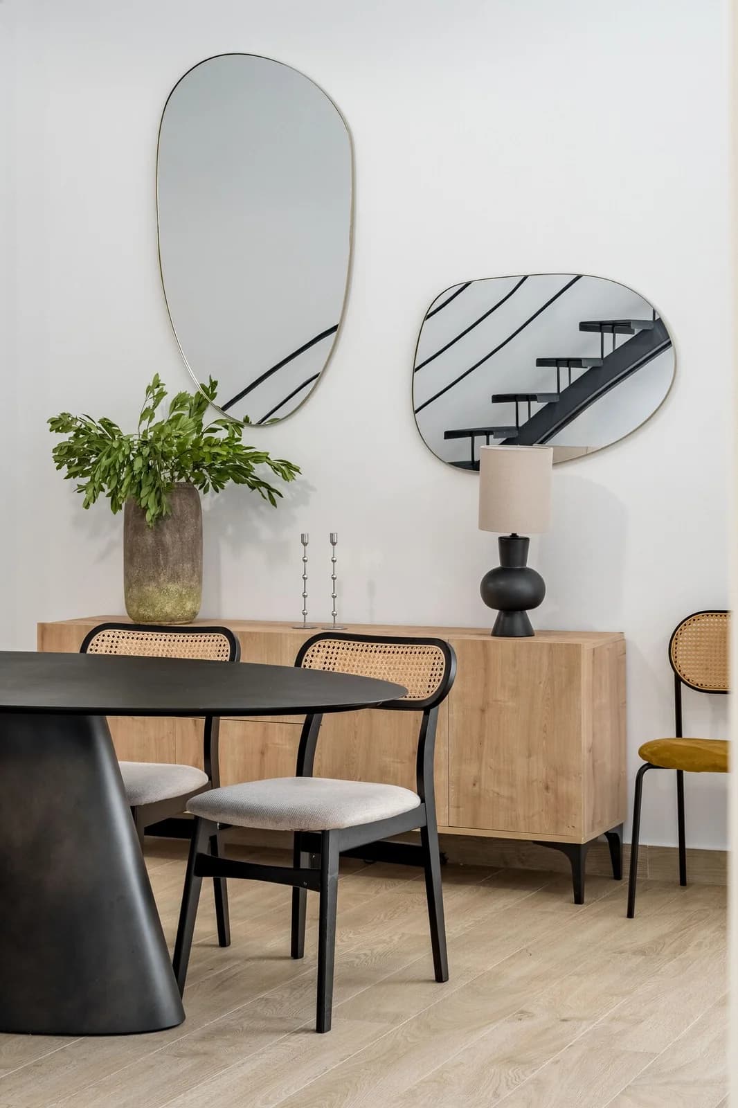 Black dining table with caned chairs reflecting the staircase in pebble mirrors