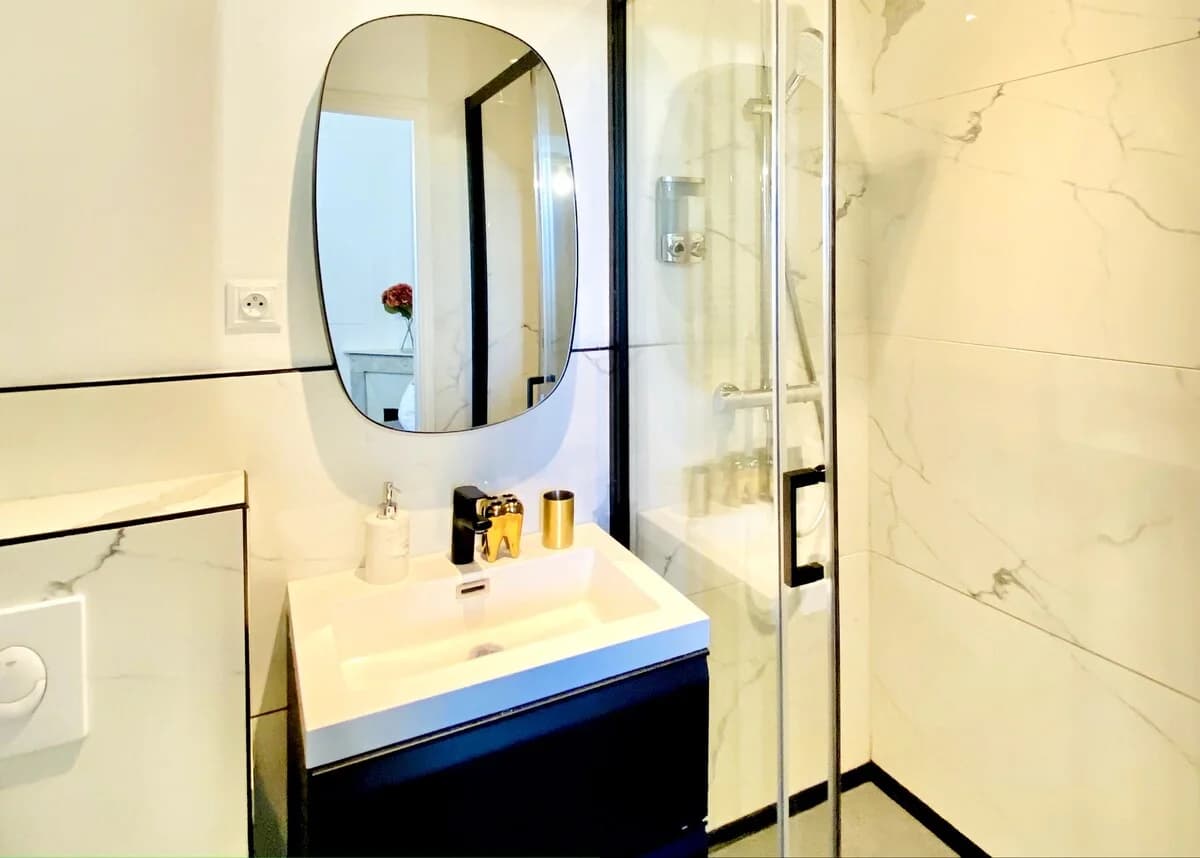 Compact ensuite with veined marble walls and oval black-rim mirror