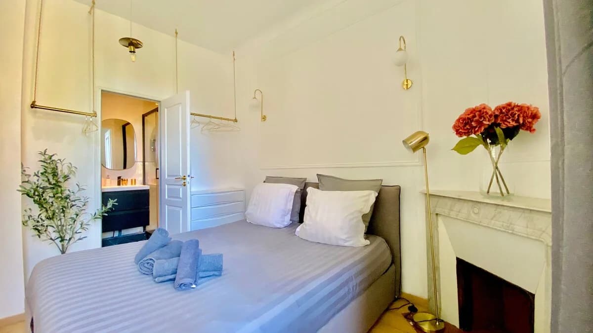Second bedroom with hanging brass rail wardrobe and ensuite bathroom beyond