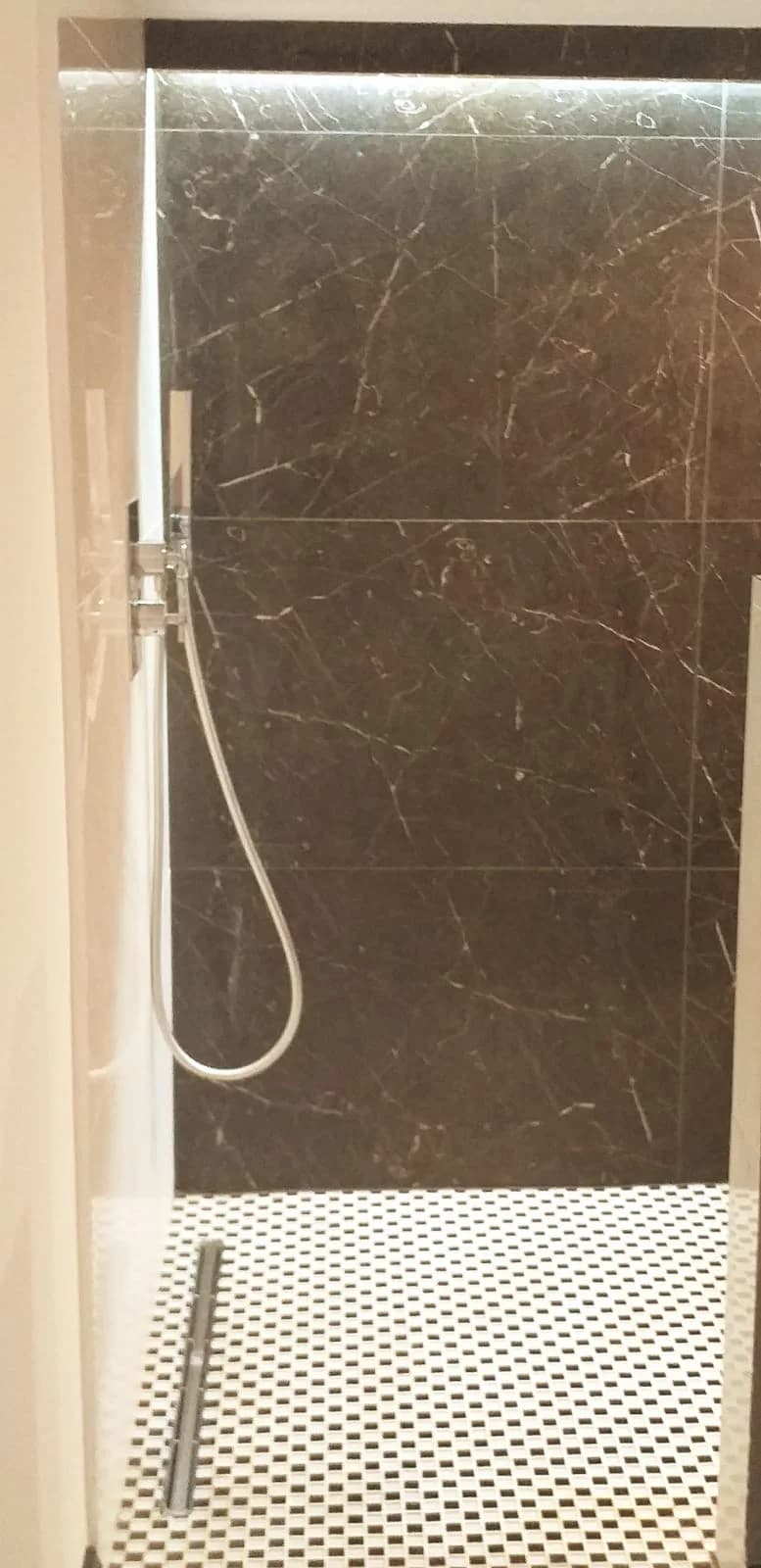Dramatic dark-marble walk-in shower over woven mosaic floor