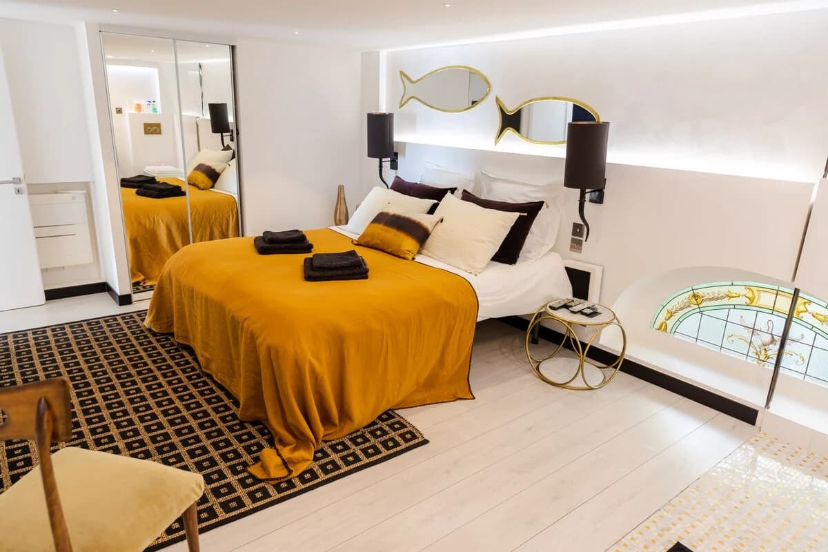Mustard-bedded room with brass fish mirrors and stained-glass arch