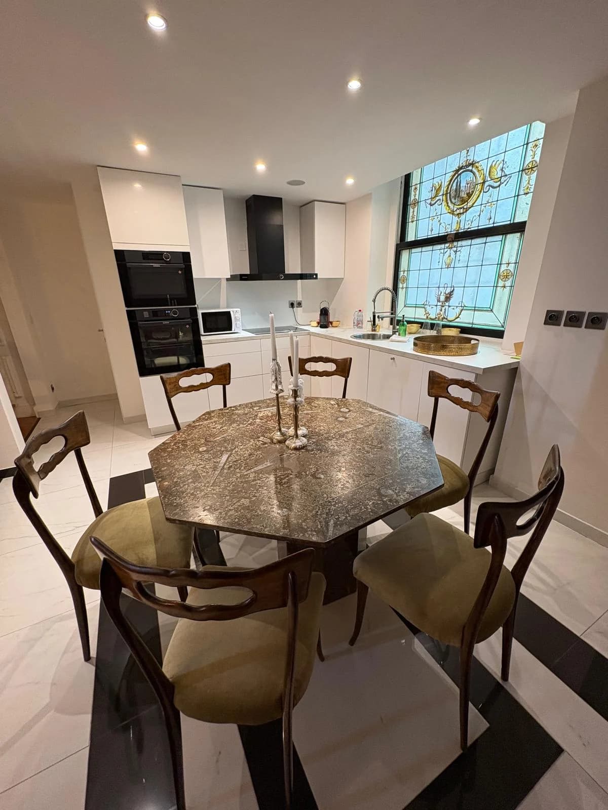 Octagonal stone dining table with gilded chairs beside the stained glass