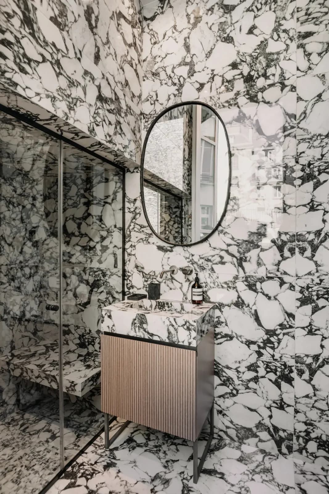 Bathroom wrapped in dramatic veined Calacatta Viola marble with oval mirror