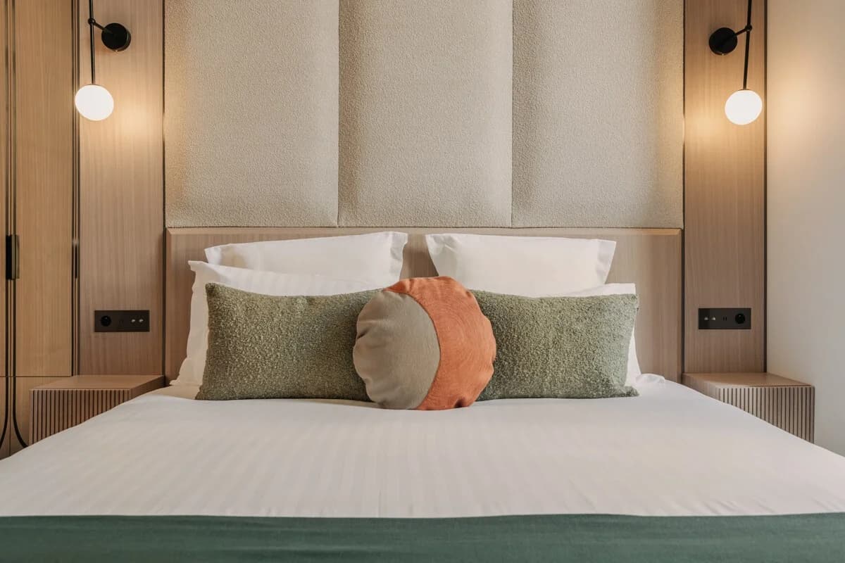 Centered bed with tactile boucle headboard and globe sconces glowing softly