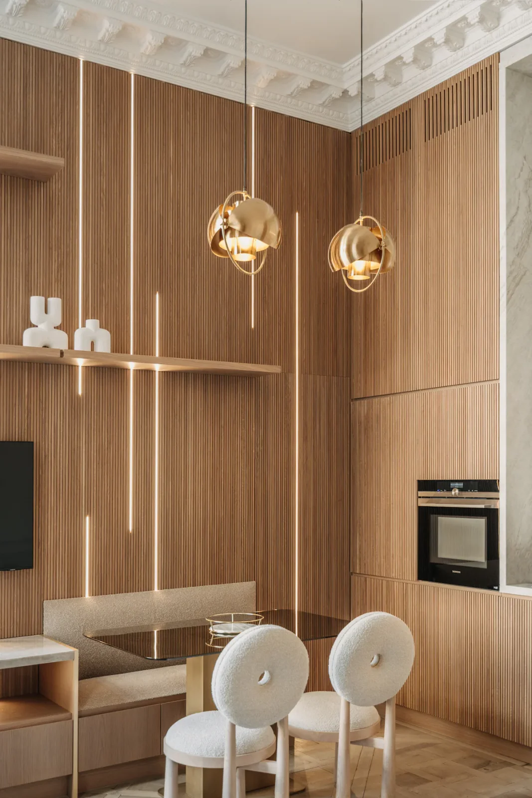Brass globe pendants over boucle chairs against fluted oak panelling