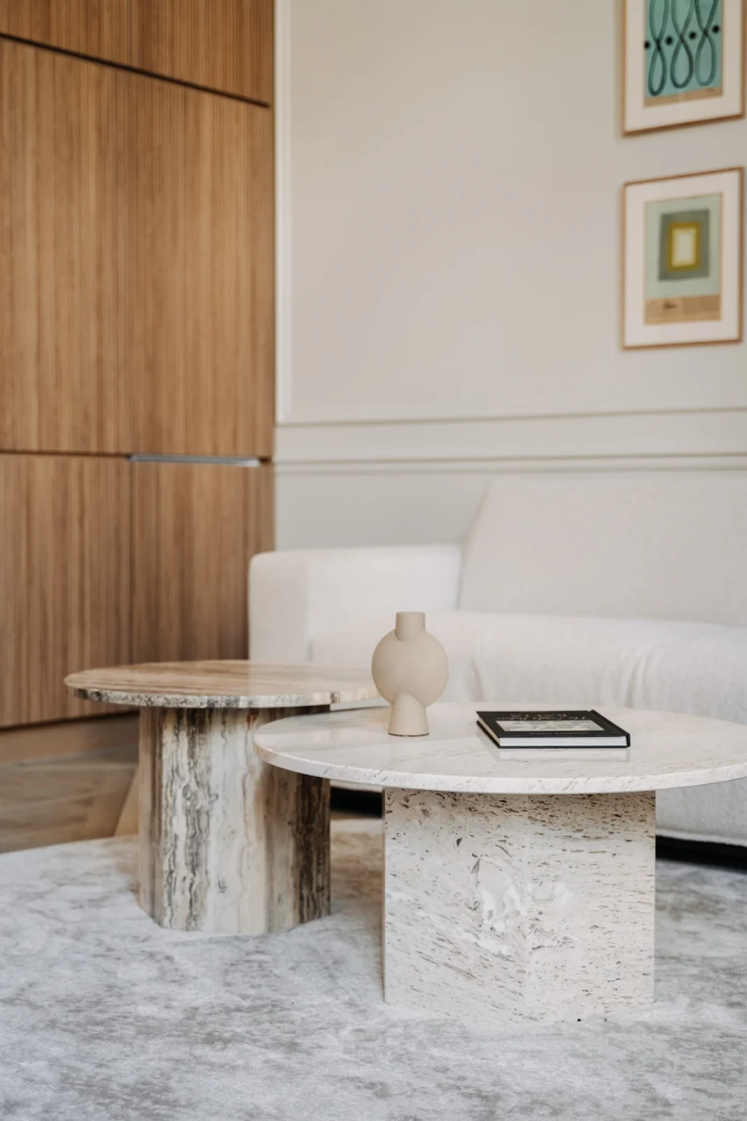 Travertine nesting tables on plush rug beside ivory boucle sofa