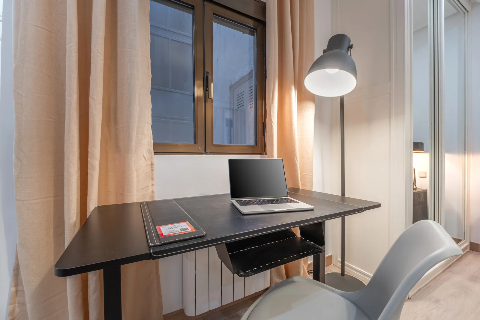 Compact desk workspace with arc lamp and curtain-framed window