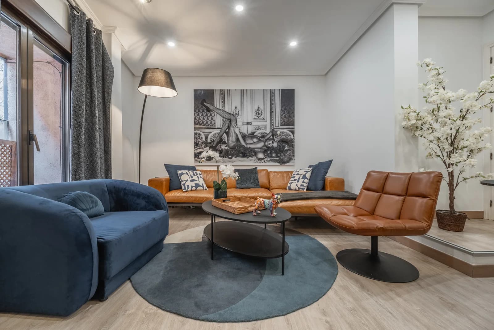 Wide lounge view across navy sofa, leather sectional, and round black coffee table