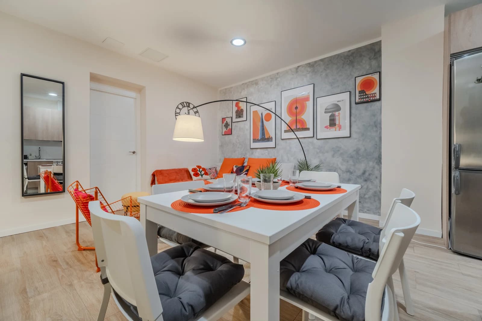 Dining table set for four under arc lamp with gallery wall behind