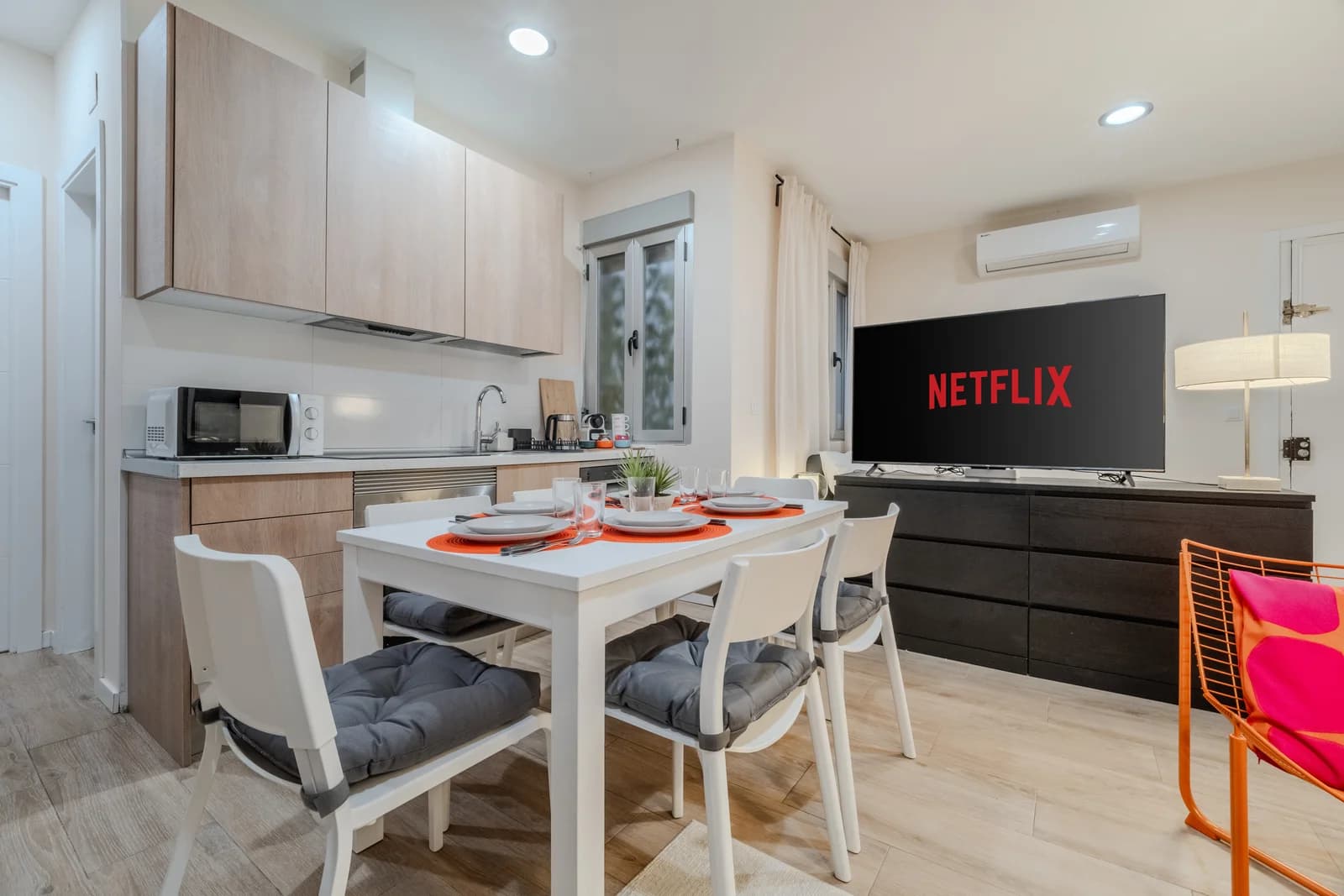 Compact kitchen with light-wood cabinetry, dining table and TV beyond