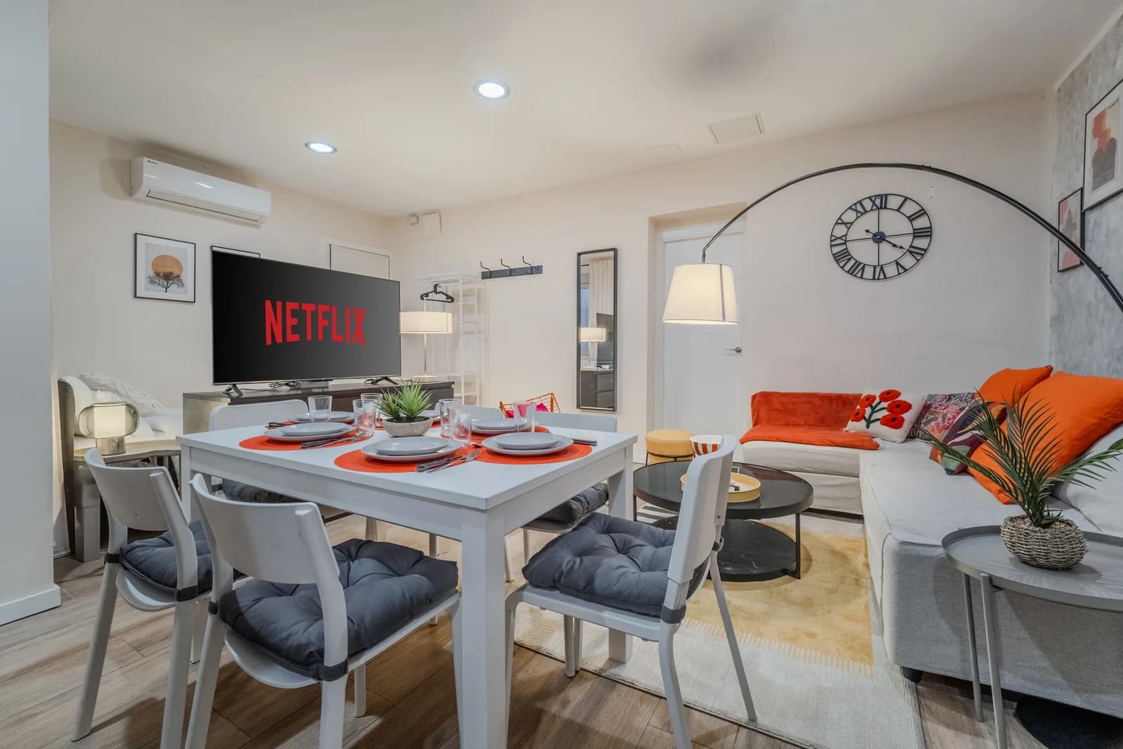 Living seating beside dining table with oversized clock and orange accents