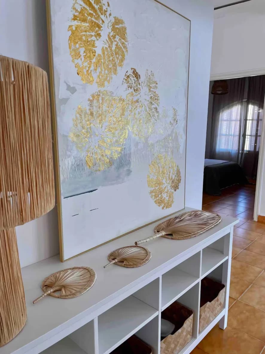 Gold-leaf artwork above console with woven palm fan accents