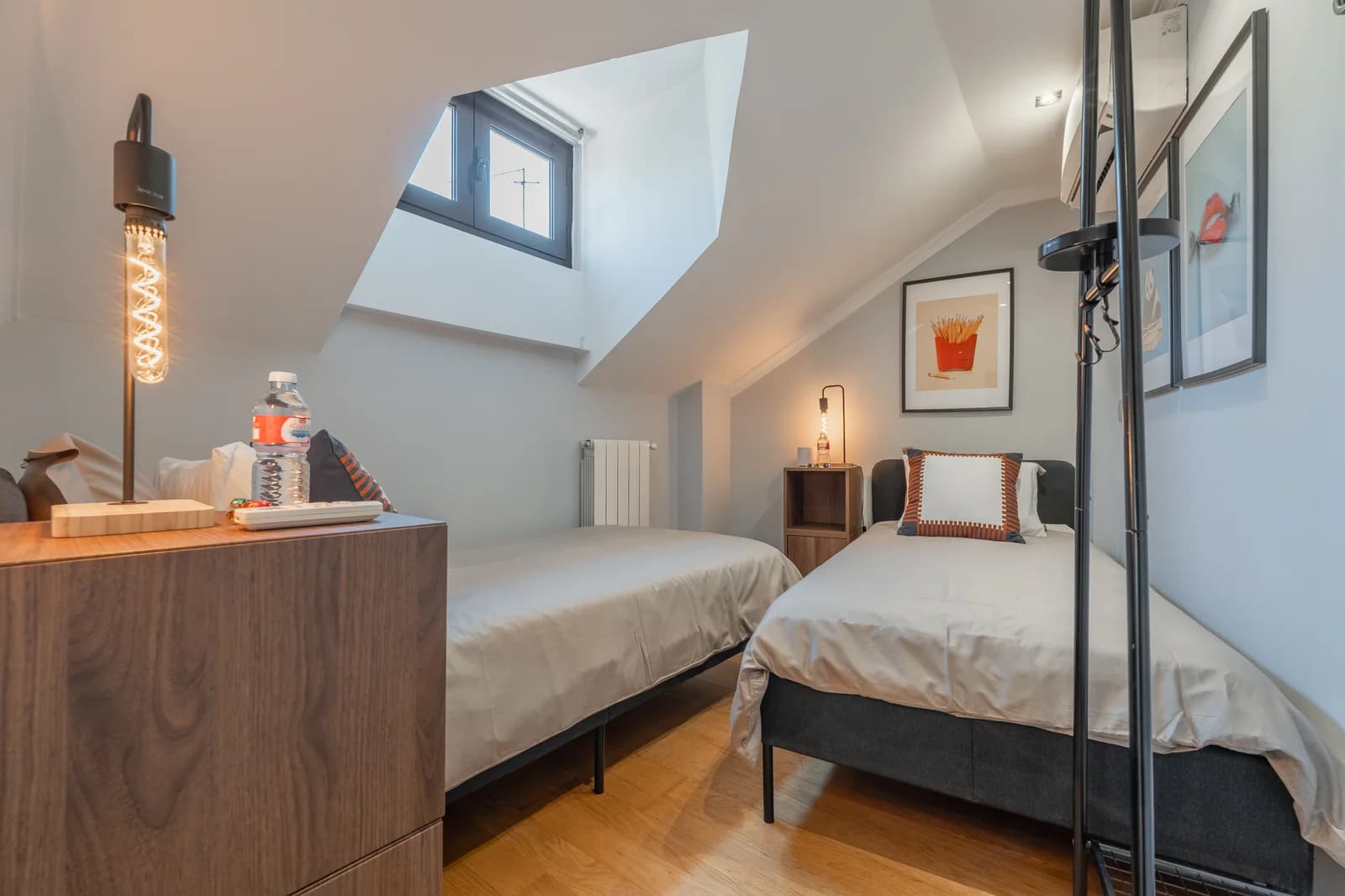 Twin-bed room under sloped ceiling with warm Edison lamp glow