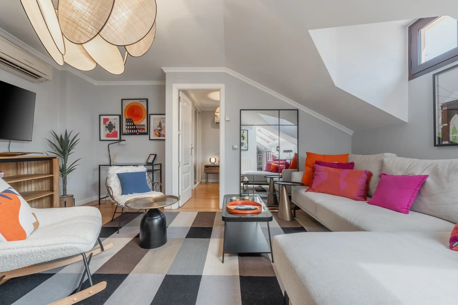 Sloped-ceiling lounge with checkerboard rug and pop colour cushions