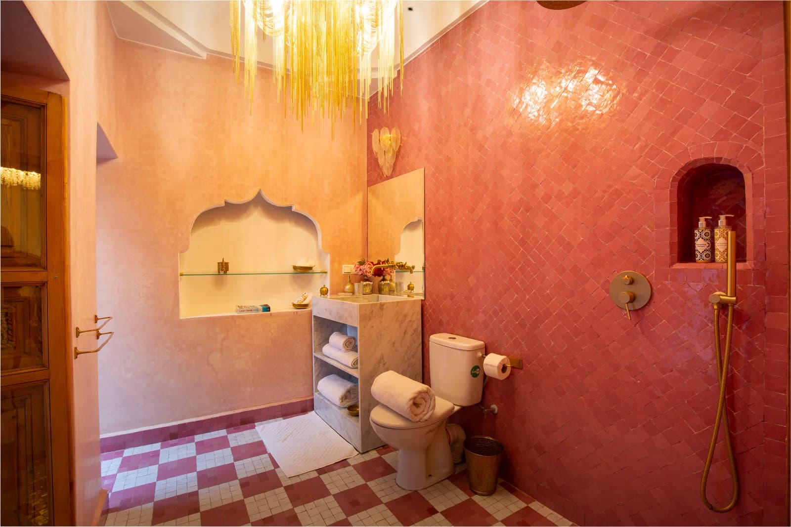 Rose-pink tadelakt bathroom with golden chandelier and zellige floor
