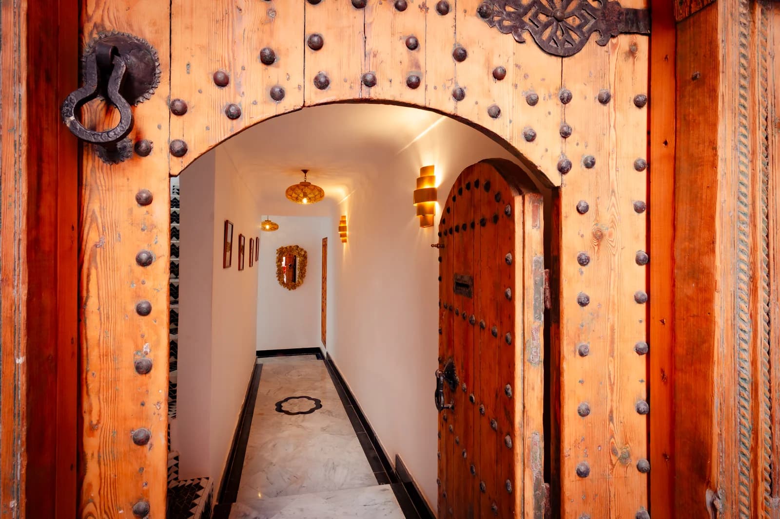 Studded wooden riad entry door with brass-knocker and lantern hallway