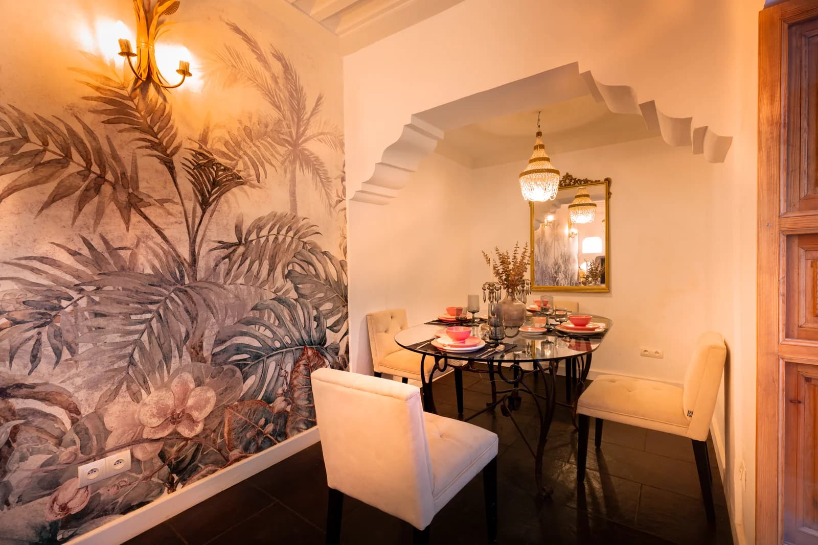 Dining nook framed by tropical mural with chandelier and gold mirror
