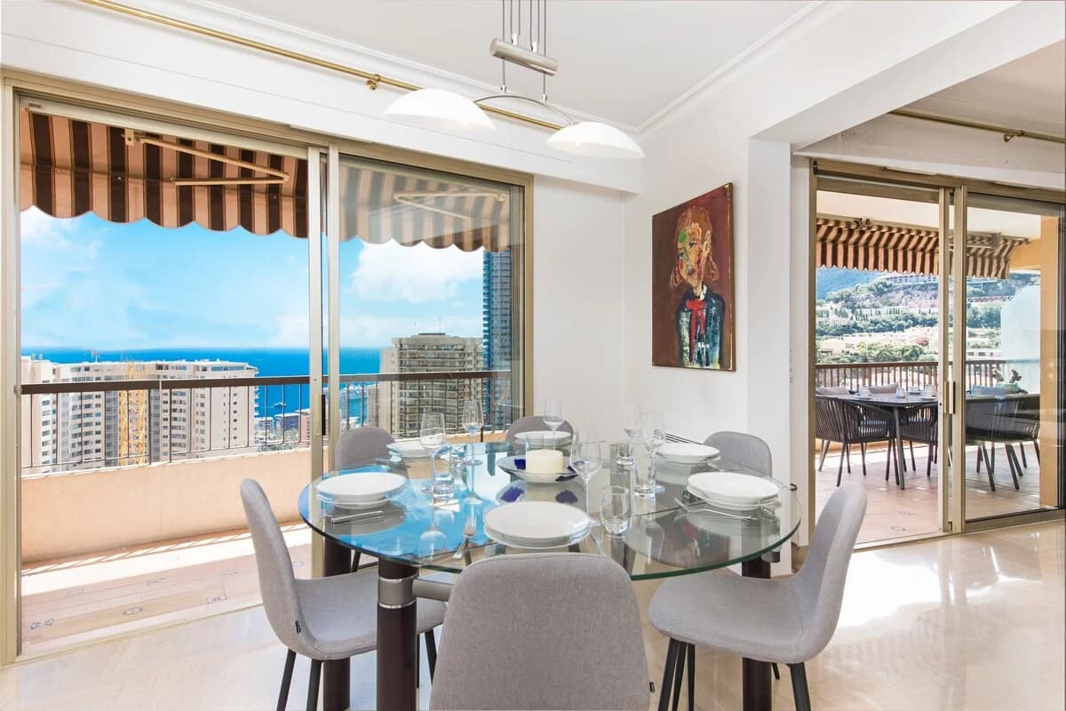 Glass dining table by floor-to-ceiling windows opening to terraces