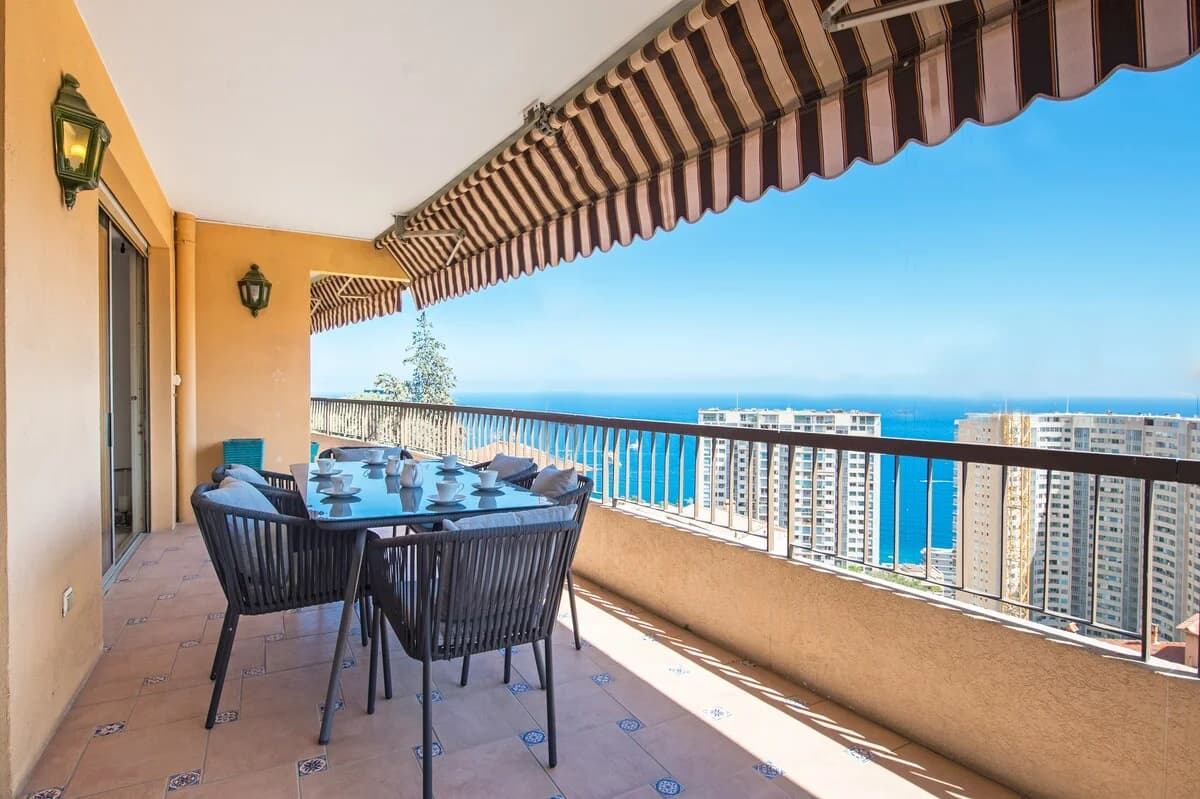 Striped-awning balcony dining table with Mediterranean sea panorama