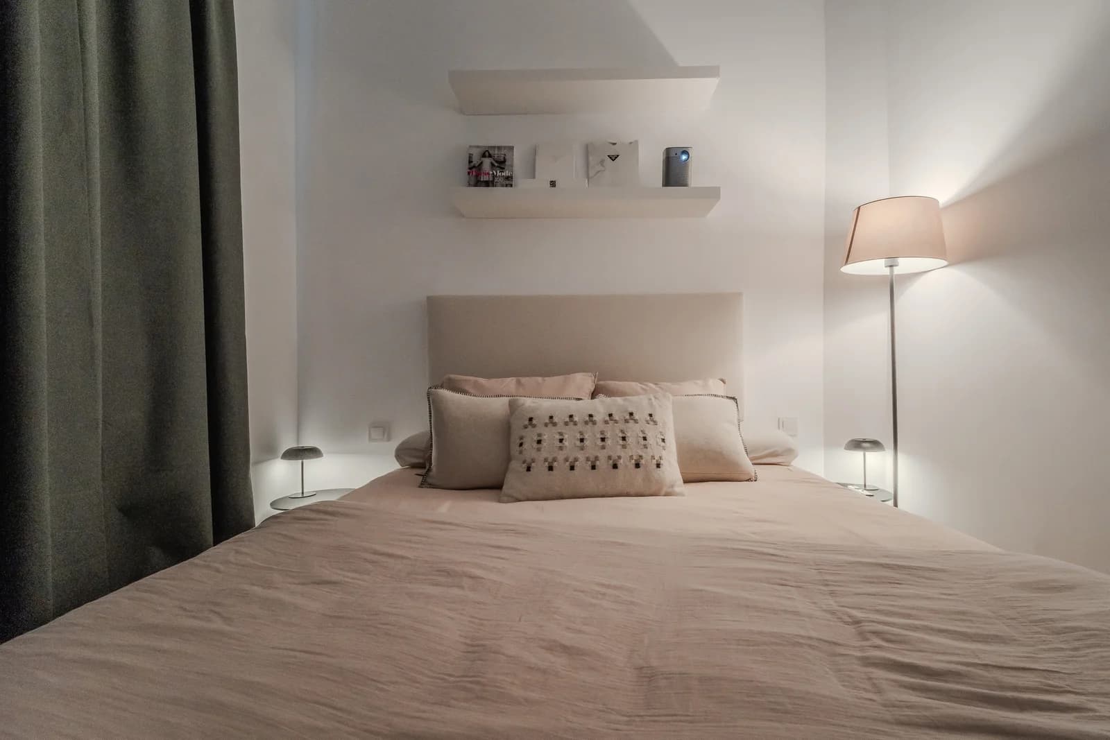 Soft pink-toned bedroom with floating shelves and warm lamplight