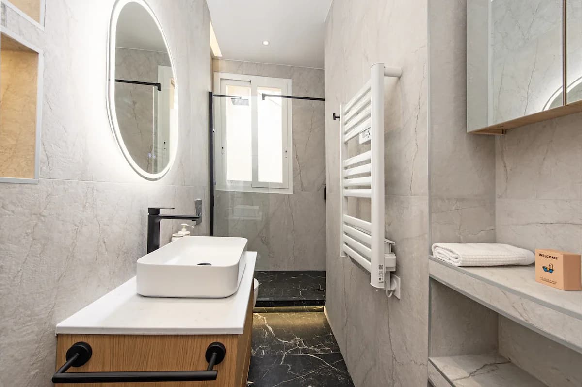 Marble bathroom with oval backlit mirror and walk-in shower
