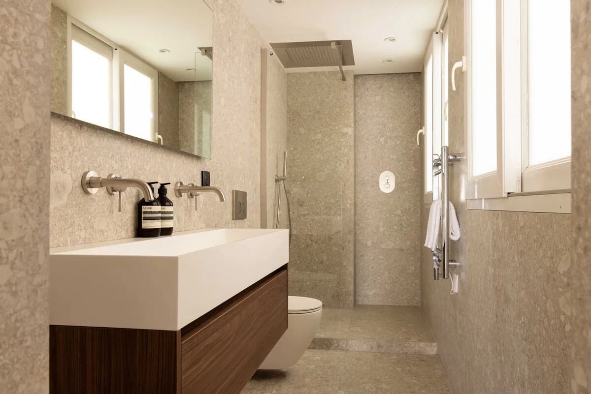 Long stone bathroom with walnut vanity, twin sinks and rain shower