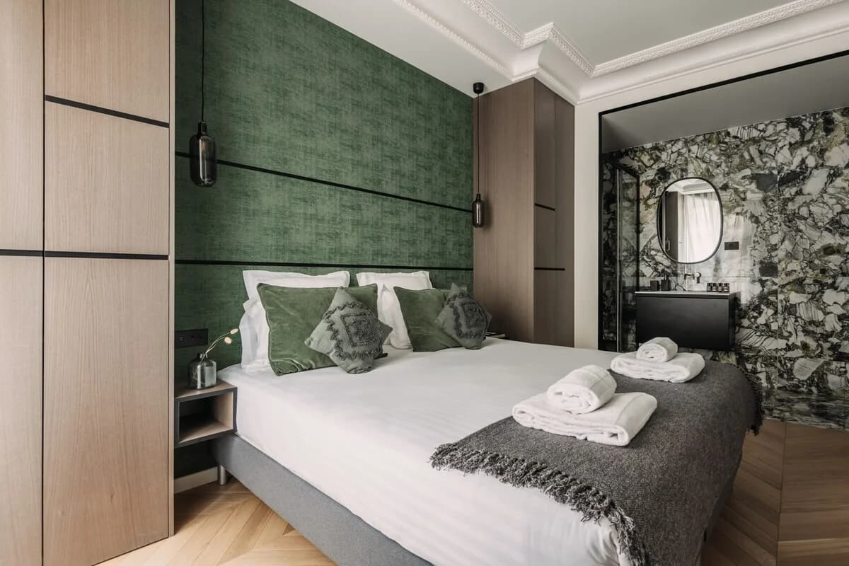 Green-textured headboard bedroom opening to dramatic marble bathroom