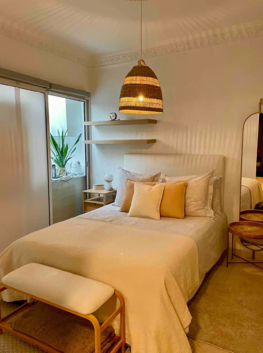 Warm bedroom with rattan pendant, ochre cushions and bench