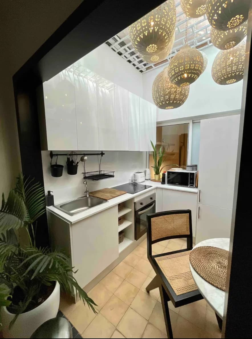 Compact white kitchen beneath skylit ceiling with rattan pendants