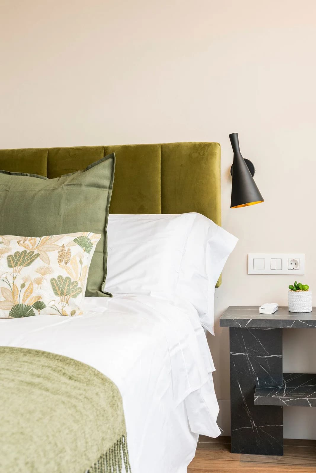 Olive velvet headboard, marble nightstand, layered linens in soft daylight