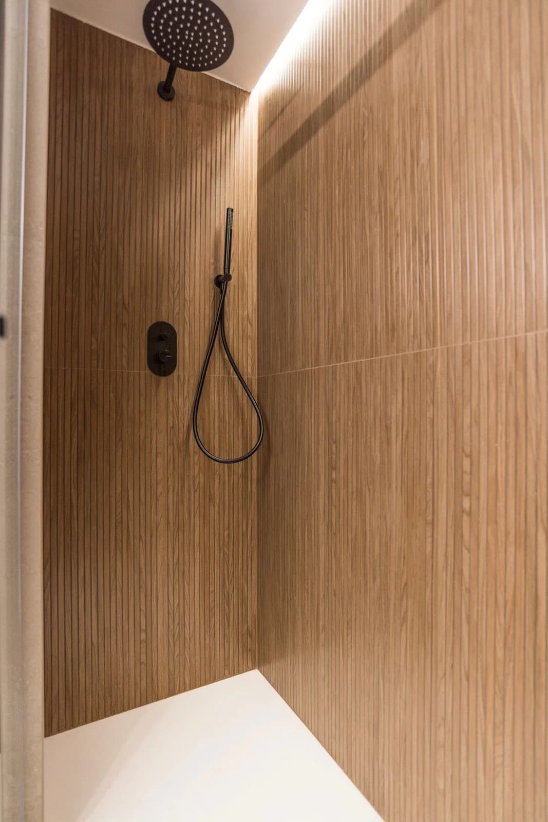 Black rainfall shower against ribbed oak panelling, sculptural and quiet