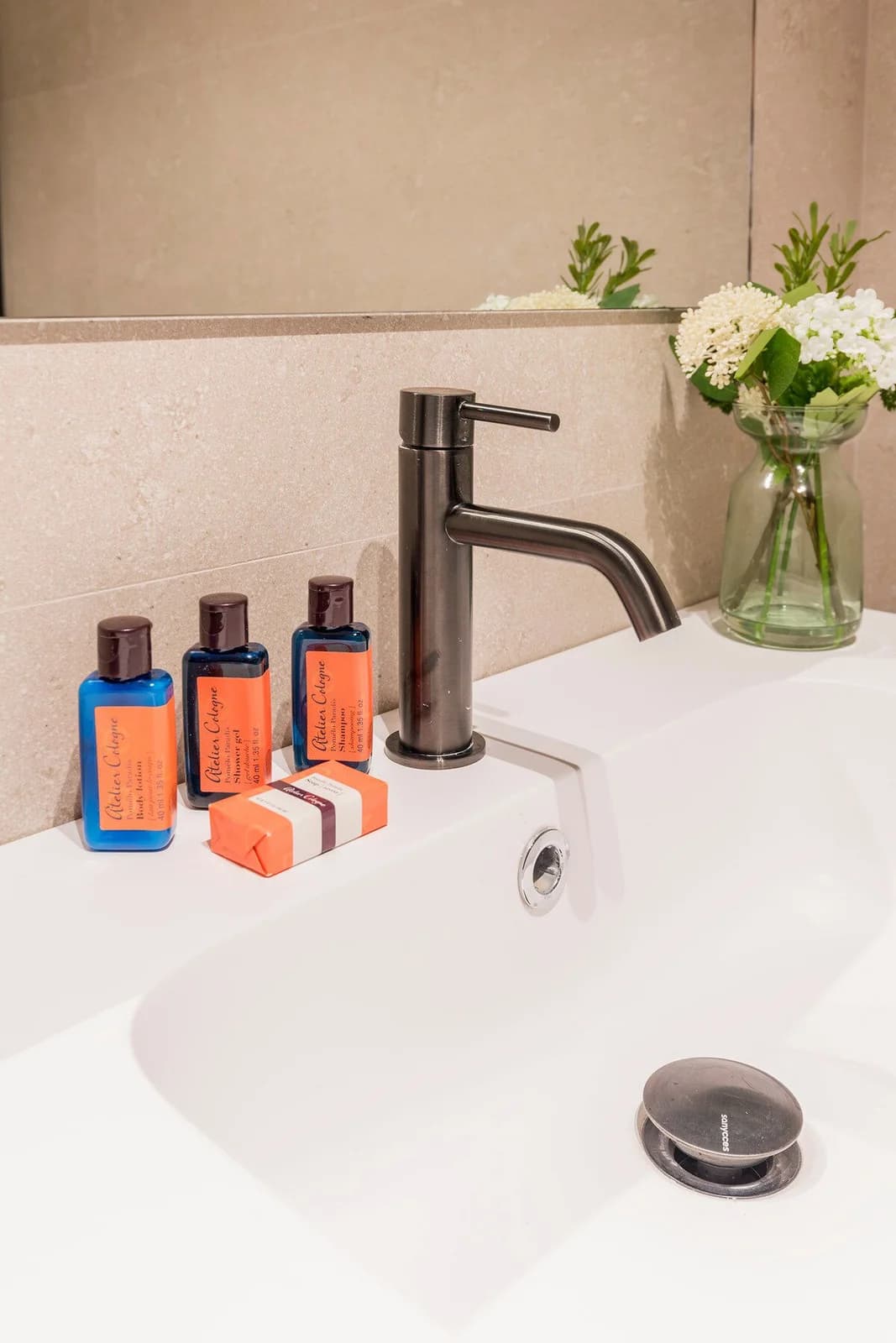 Atelier Cologne amenities arranged beside the basin and fresh blooms