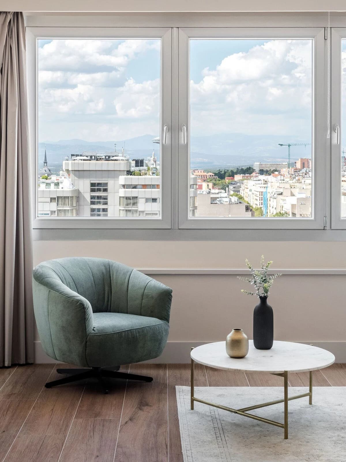 Velvet armchair framing wide Madrid rooftop and mountain panorama