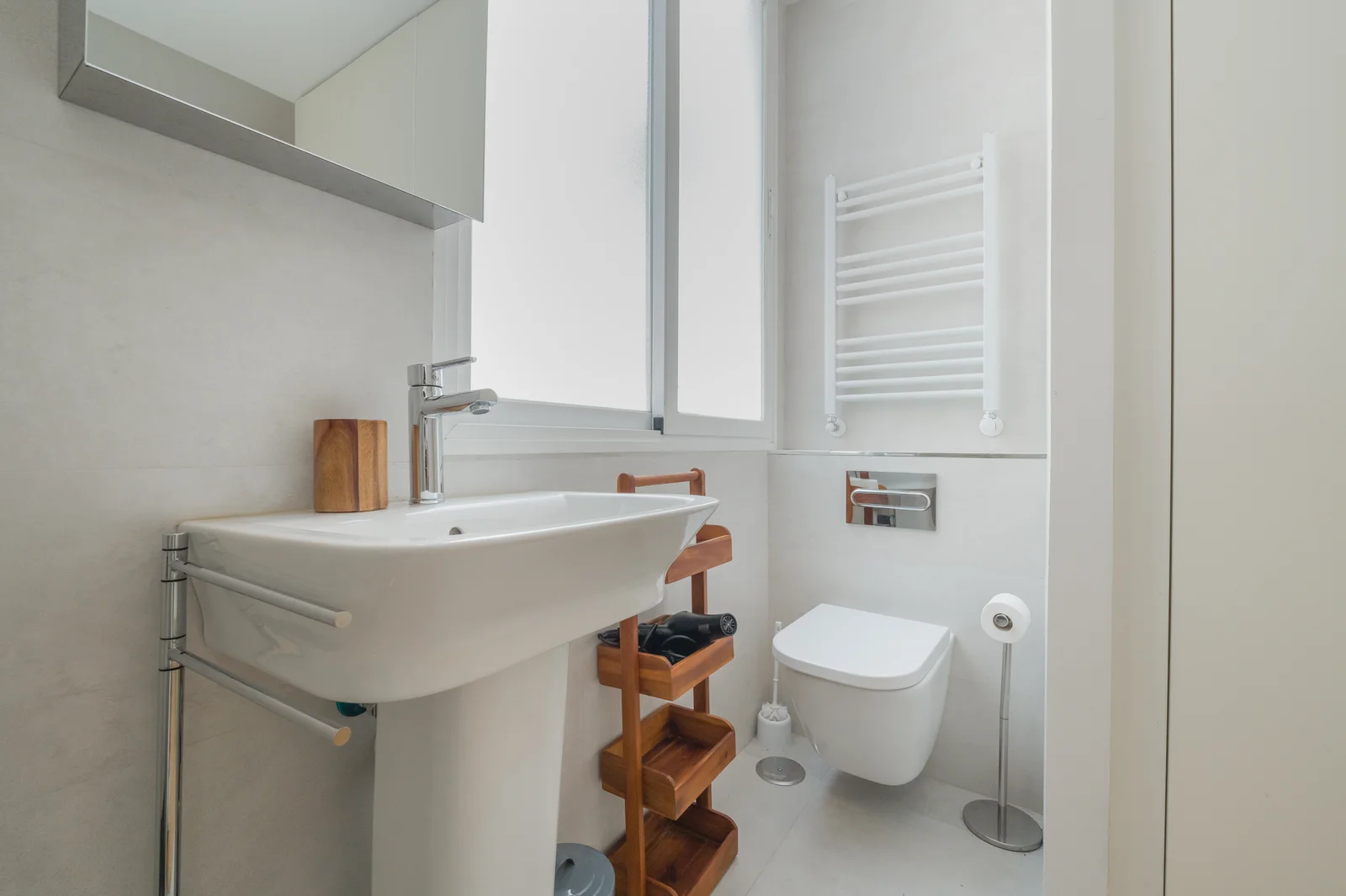 Bright white bathroom with pedestal sink and wooden accents