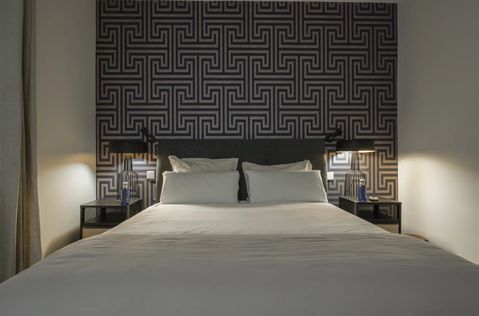 Geometric Greek-key wallpaper headboard wall lit by twin lamps