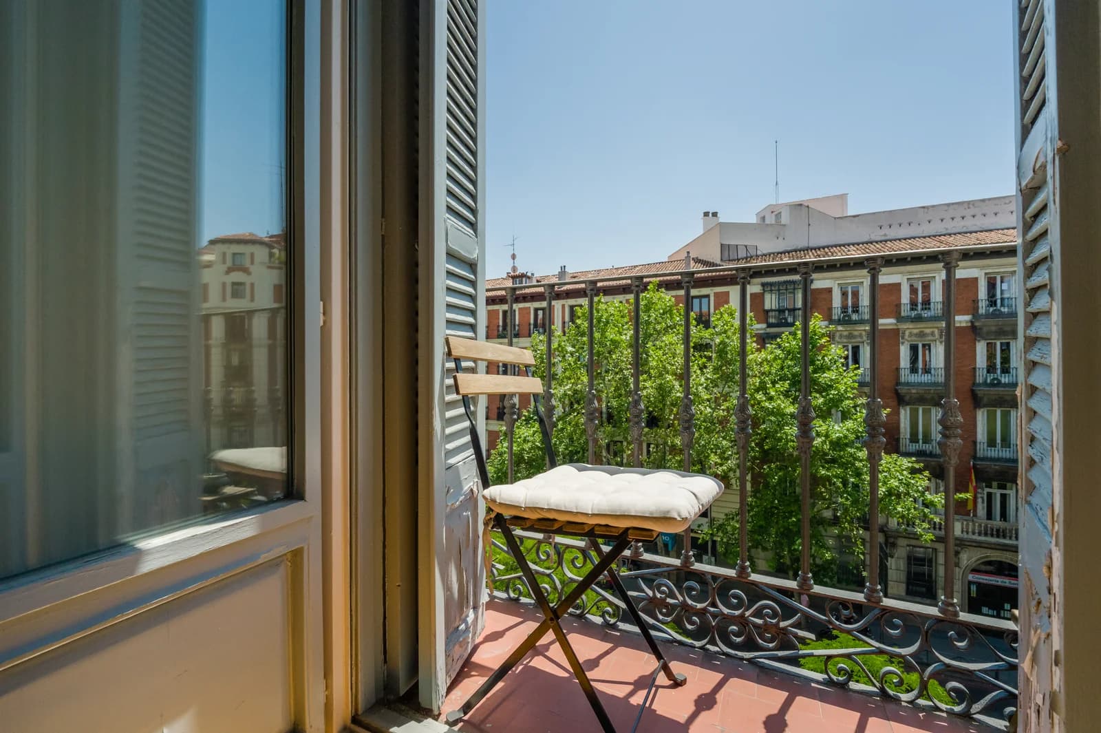 Wrought-iron Madrid balcony framed by trees and sun-warmed shutters