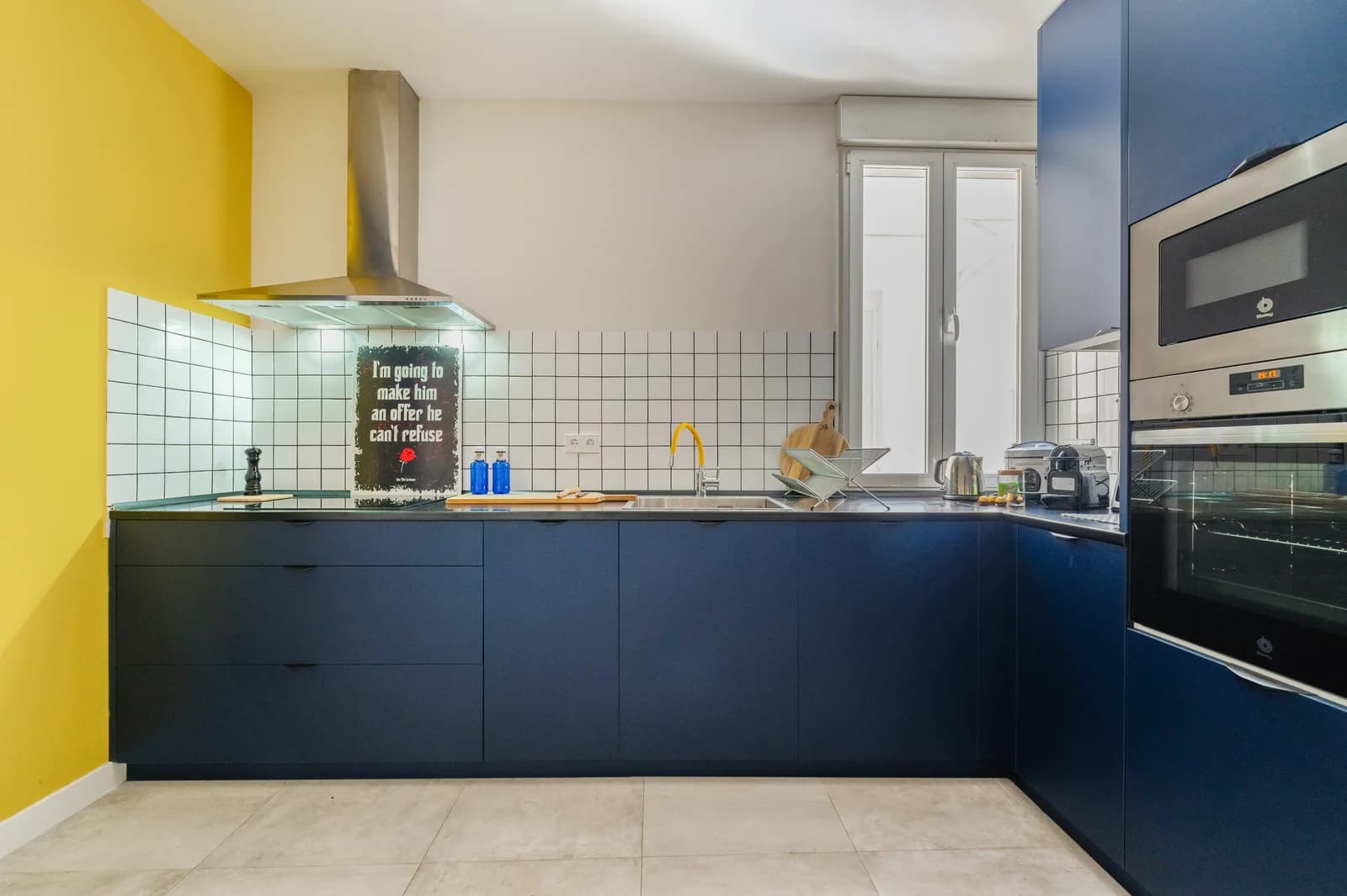 L-shaped navy kitchen with white tile splashback and yellow accent wall