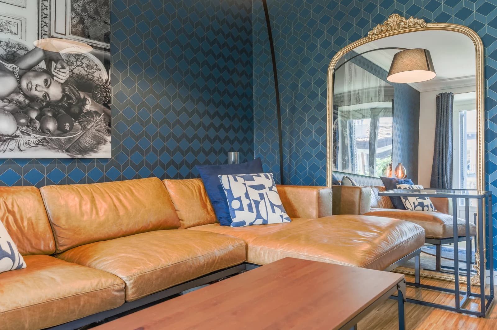 Tan leather sofa against blue patterned wallpaper and gilded mirror
