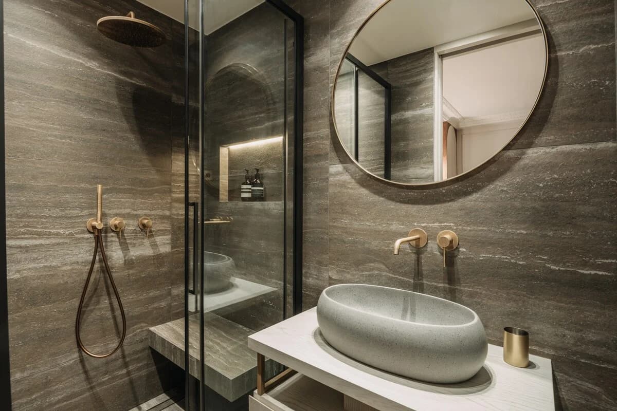 Travertine en-suite with brass shower, oval mirror, pebble basin
