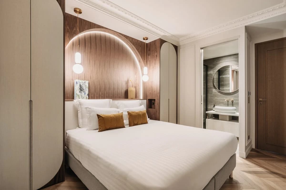 Walnut arch with backlit halo, ochre cushions, en-suite glimpse beyond