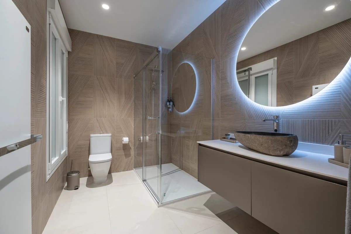 Geometric oak wall, stone vessel sink, halo-lit round mirror