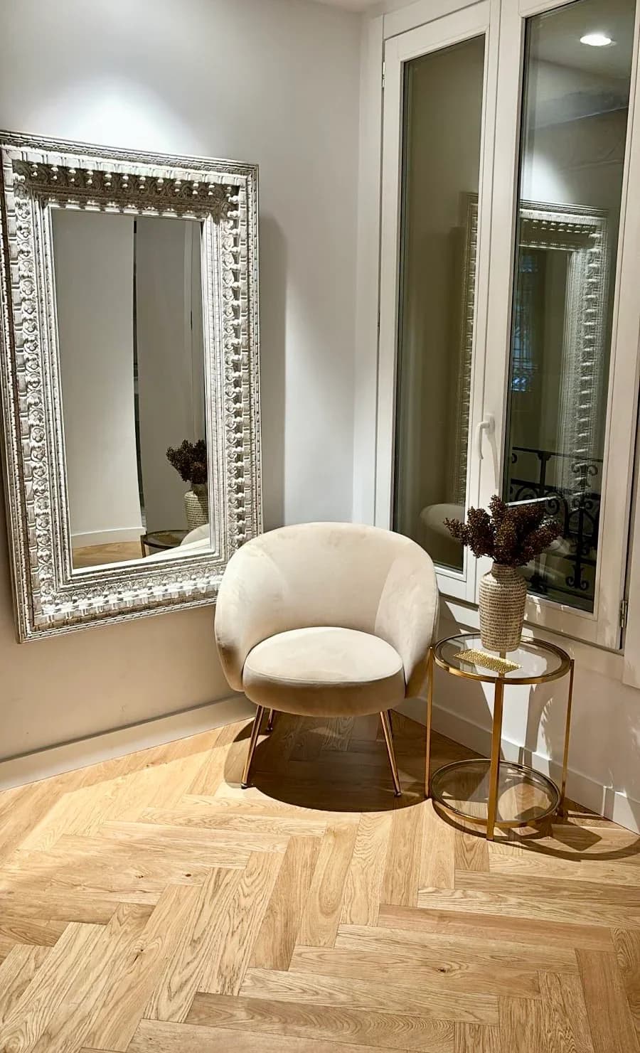 Silver-framed mirror over velvet armchair on chevron parquet
