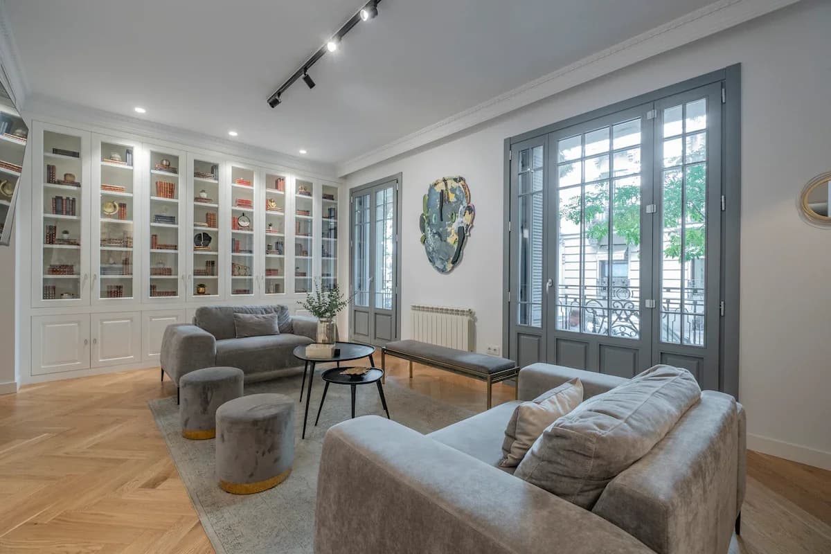 Library wall of glass cabinets above herringbone floor and grey velvets