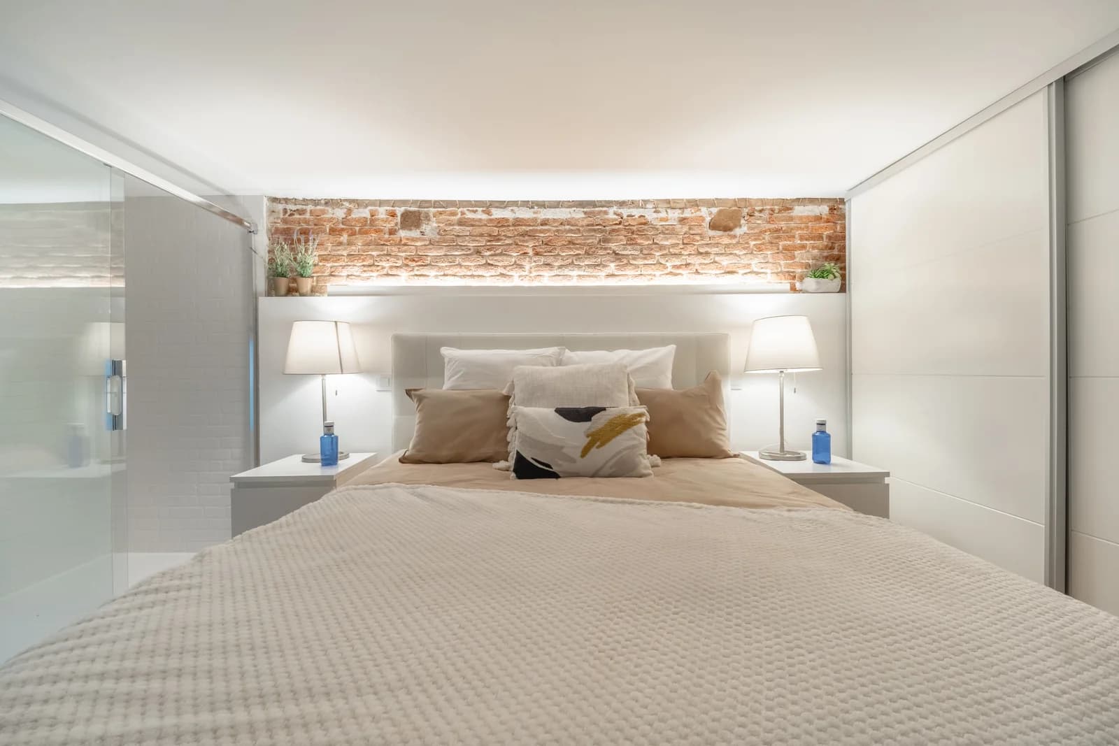 Mezzanine bedroom with exposed brick band and twin lamps