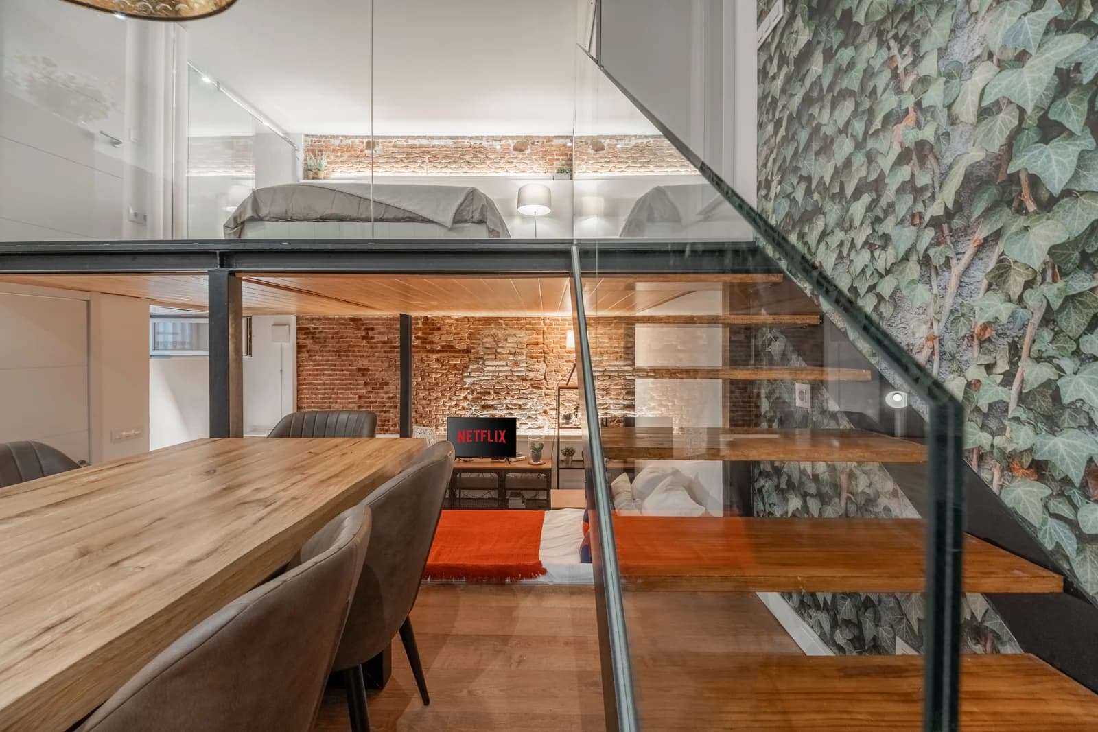 Glass-balustrade staircase rising past brick to the mezzanine bed
