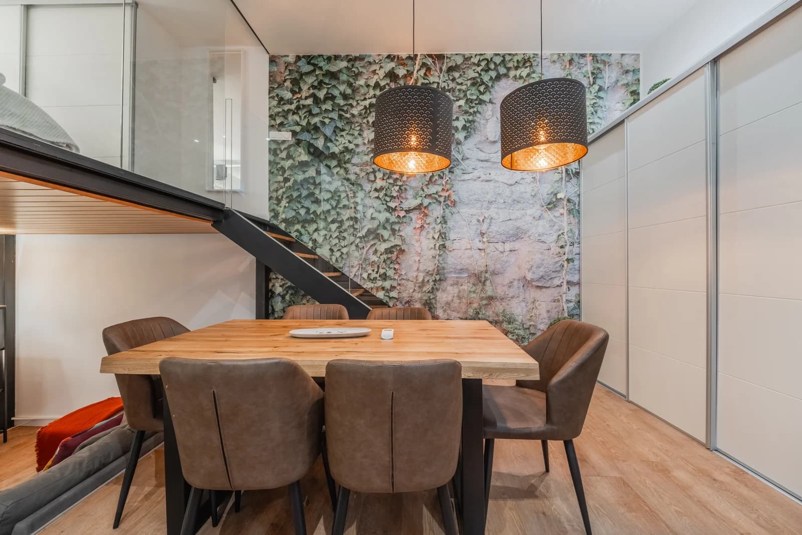 Dining table beneath rattan pendants framed by ivy mural