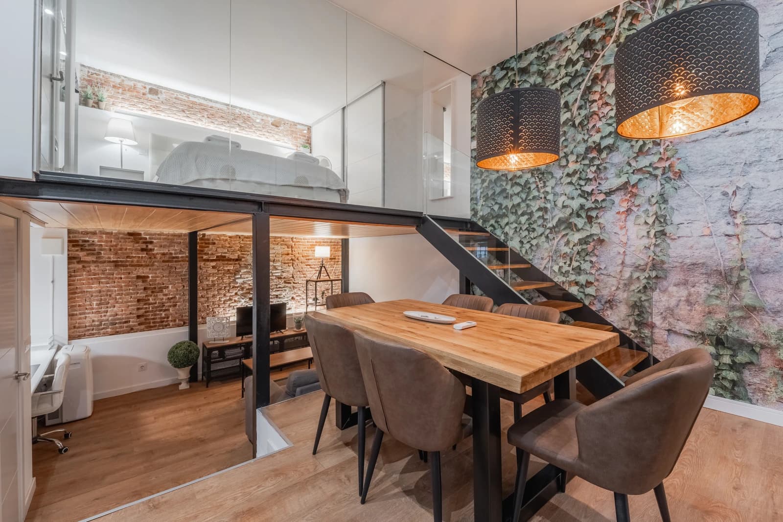 Dining table beneath black pendants with ivy mural and mezzanine bedroom above